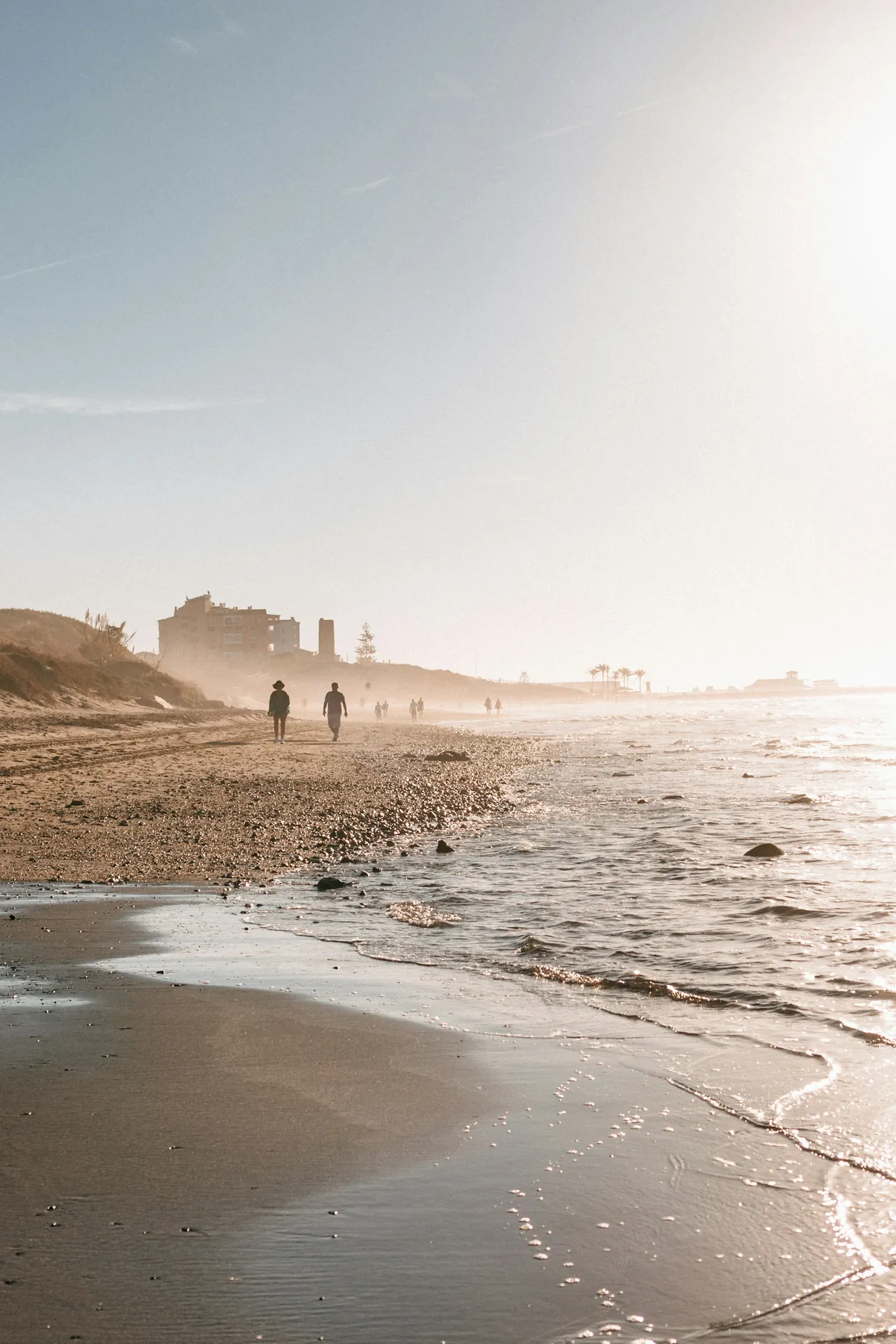 Two people walking along the misty shoreline of Cabopino beach