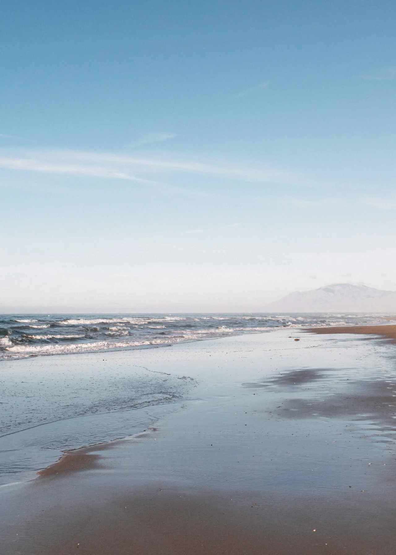 Wet sand and gentle waves on Cabopino beach under a blue sky
