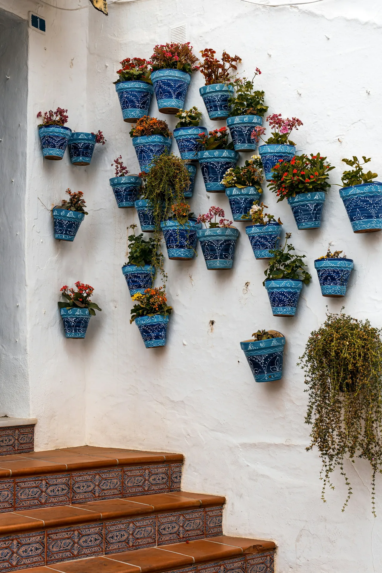 Blue flower pots on a white wall beside tiled steps in Mijas Pueblo