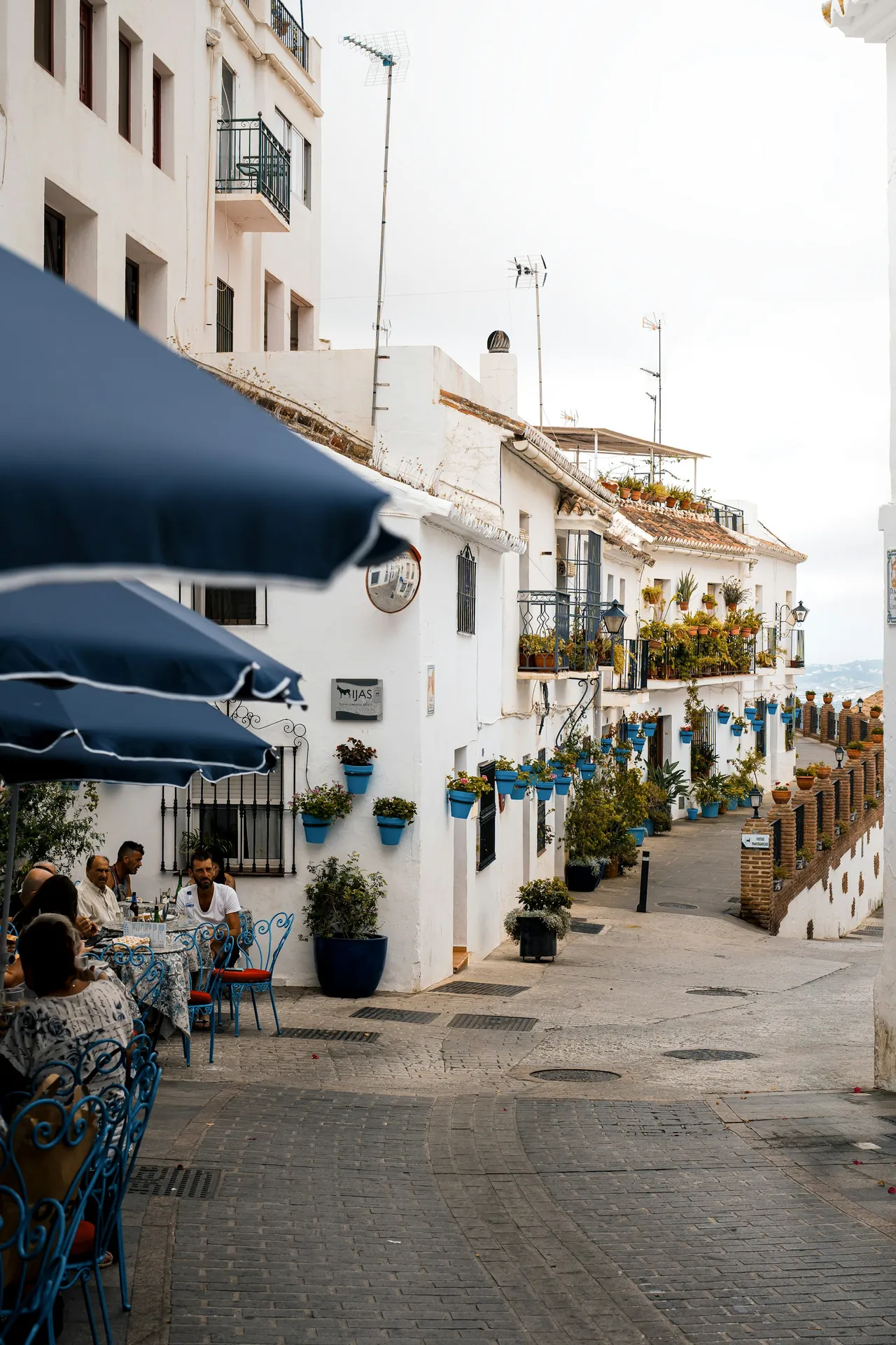 A white street with restaurant terraces and blue flower pots in Mijas Pueblo