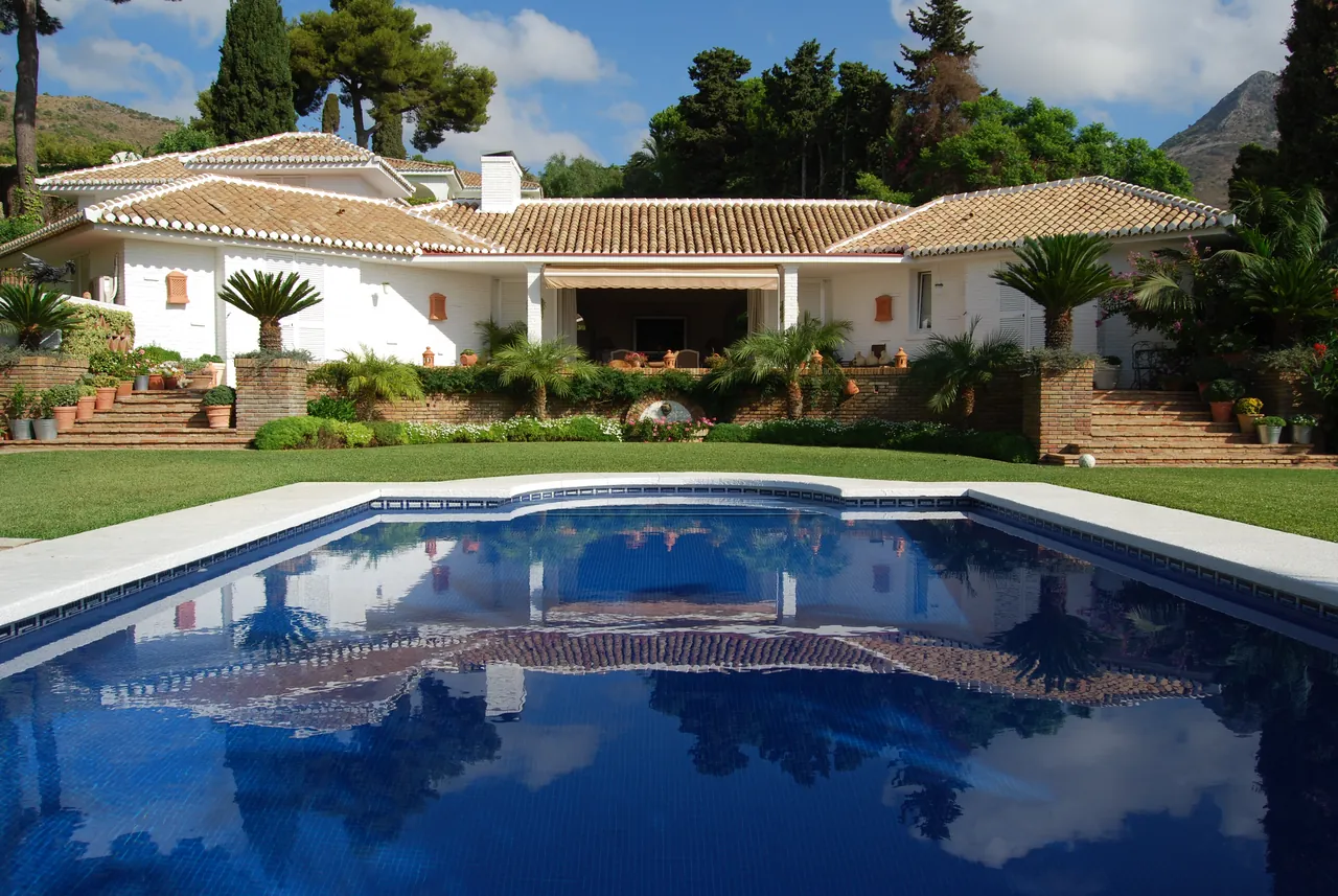 A white villa with a tiled roof and a blue pool